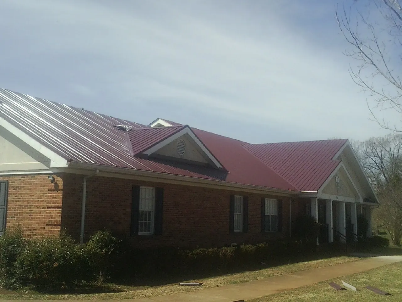Red metal roof with gabled entries on a long brick building, from a Hail Damage Roof Repair job in Frankford