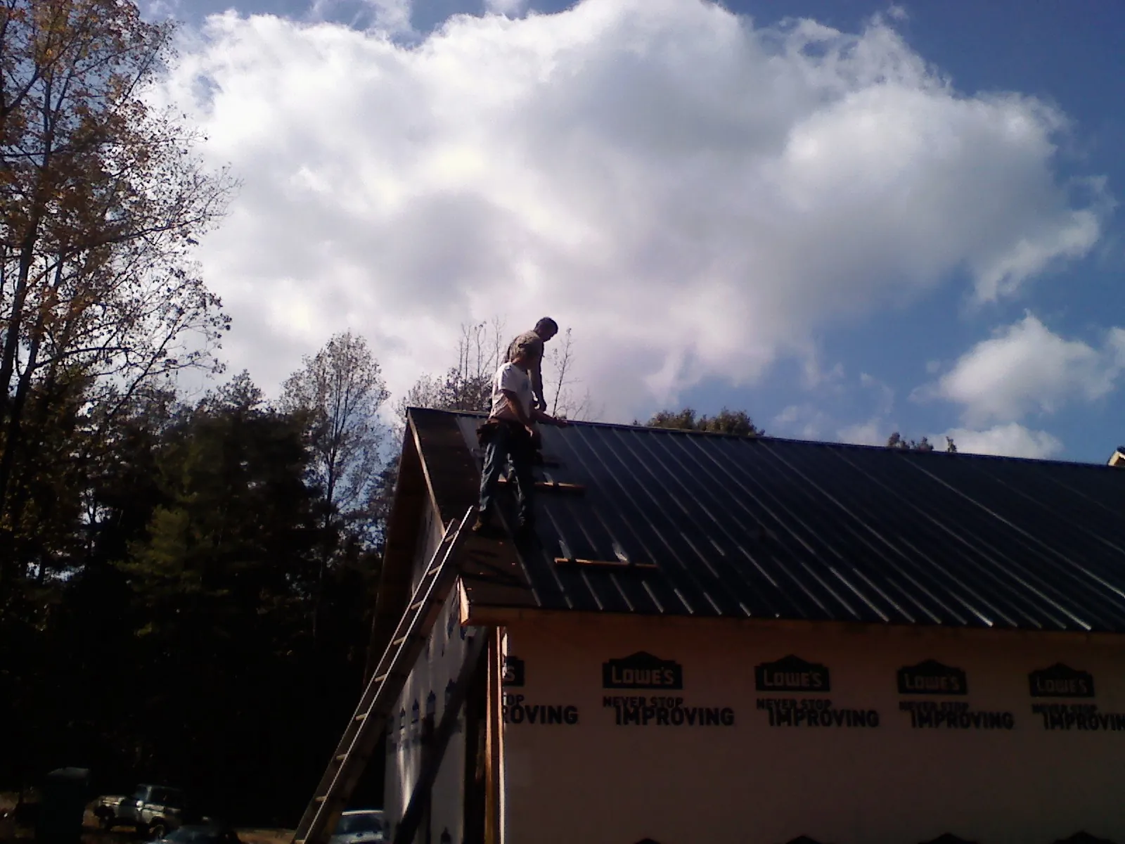 Roofer fastening dark metal panels high against a cloudy sky, from a Roof Inspection job in Frankford