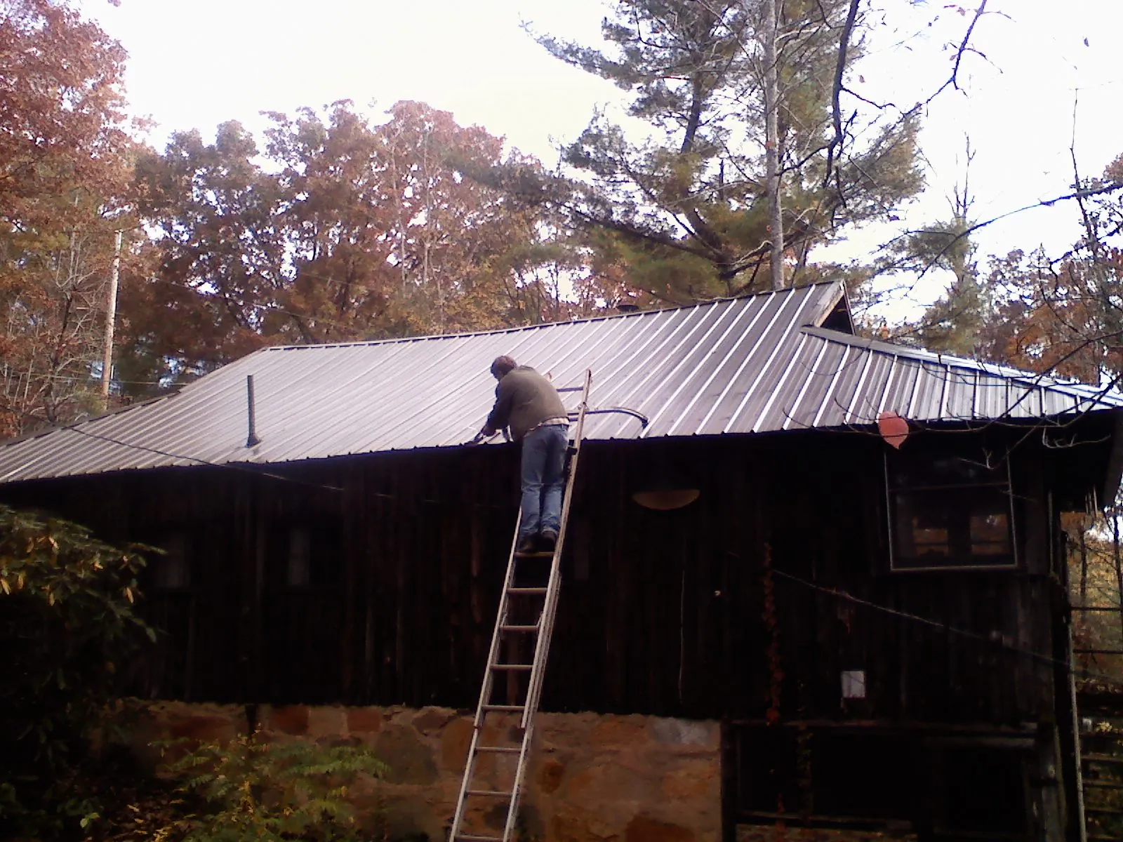 Roofer on a ladder working along the edge of a cabin metal roof in Frankford