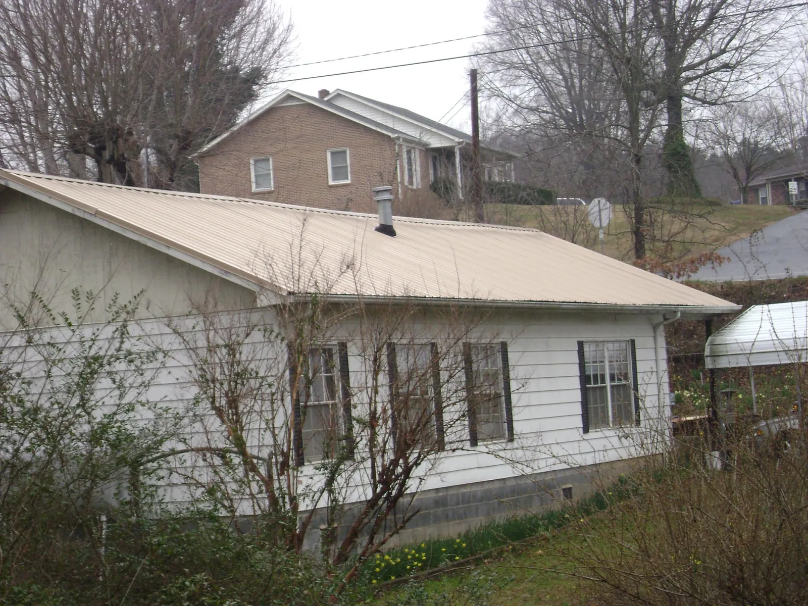 Tan metal roof on a white sided house set into a hillside — Commercial Roofing by Roofing Brothers in Frankford